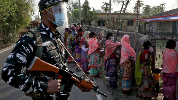 An armed policeman wearing a face shield stands guard as women wait in line to cast their votes outside a polling booth during the first phase of the West Bengal state election in Purulia district, India, March 27, 2021 - Sputnik International