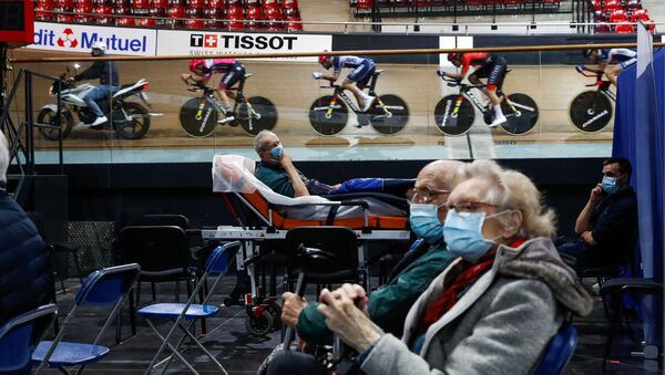 France's national cycling team trains as people wait to get a dose of the Comirnaty Pfizer-BioNTech COVID-19 vaccine as part of the coronavirus disease vaccination campaign at the indoor Velodrome National of Saint-Quentin-en-Yvelines in Montigny-le-Bretonneux, southwest of Paris, France, March 26, 2021 - Sputnik International
