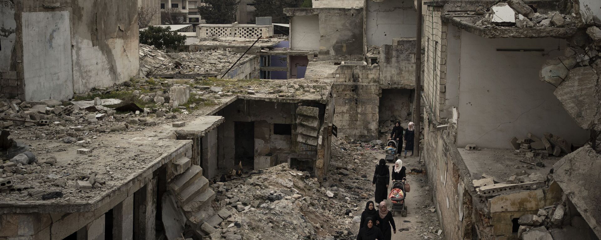 In this March 12, 2020 file photo, women walk in a neighborhood heavily damaged by airstrikes in Idlib, Syria. - Sputnik International, 1920, 26.04.2022