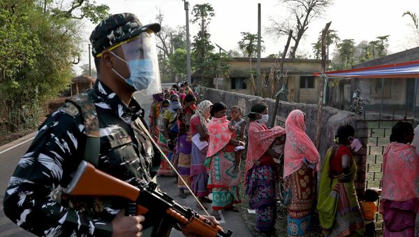 An armed policeman wearing a face shield stands guard as women wait in line to cast their votes outside a polling booth during the first phase of the West Bengal state election in Purulia district, India, 27 March 2021. - Sputnik International