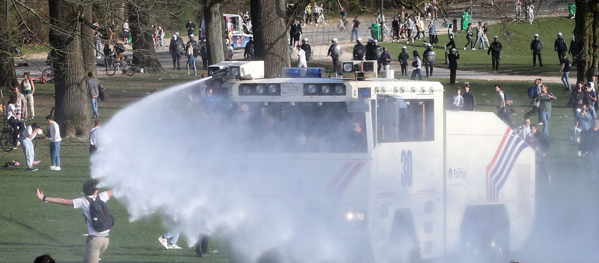 Bystanders and demonstrators are soaked by a Belgian police water canon as police officers surround them at the Bois de la Cambre parc, in Brussels, on April 1, 2021 during a unauthorised rally, for a fake concert announced on social media as an April Fool's Day prank. (Photo by Franзois WALSCHAERTS / AFP) - Sputnik International, 1920