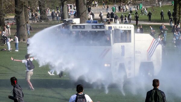 Bystanders and demonstrators are soaked by a Belgian police water canon as law enforcement officers surround them at Bois de la Cambre, in Brussels, on 1 April 2021 during an unauthorised rally and fake concert announced on social media as an April Fool's Day prank. (Photo by Franзois WALSCHAERTS / AFP) - Sputnik International