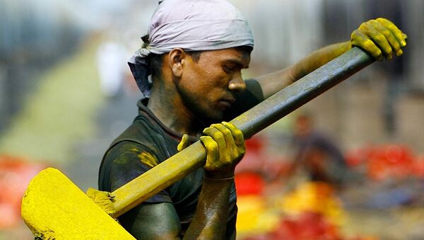 A migrant labourer using the space between municipal water pipes in Dharavi, pounds old paint chips into fine powder in Mumbai - Sputnik International