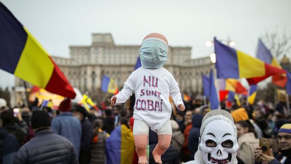 A man wearing a skull mask while dressed in white protection gear holds a baby doll with the message I am not a lab rat during a protest against mandatory mask wearing and coronavirus disease (COVID-19) vaccination, near the Romanian Parliament, in Bucharest, Romania March 20, 2021. - Sputnik International