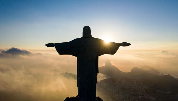 The sun rises in front of the Christ the Redeemer statue in Rio de Janeiro on March 24, 2021. - Christ the Redeemer is celebrating its 90th anniversary in October 2021 and is receiving restoration work to ensure that it looks its best for the public and visiting tourists. - Sputnik International