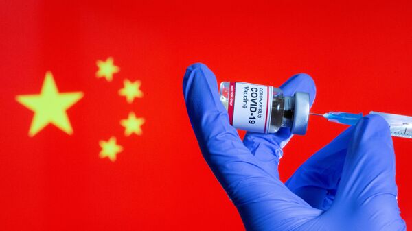 FILE PHOTO: FILE PHOTO: A woman holds a small bottle labeled with a Coronavirus COVID-19 Vaccine sticker and a medical syringe in front of displayed China flag in this illustration taken, October 30, 2020 - Sputnik International