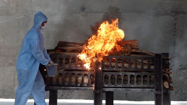 A frontline worker in personal protective equipment (PPE) sprays a flammable liquid on a burning funeral pyre of a man who died from the coronavirus disease  (COVID-19), at a crematorium on the outskirts of Mumbai India, April 15, 2021 - Sputnik International
