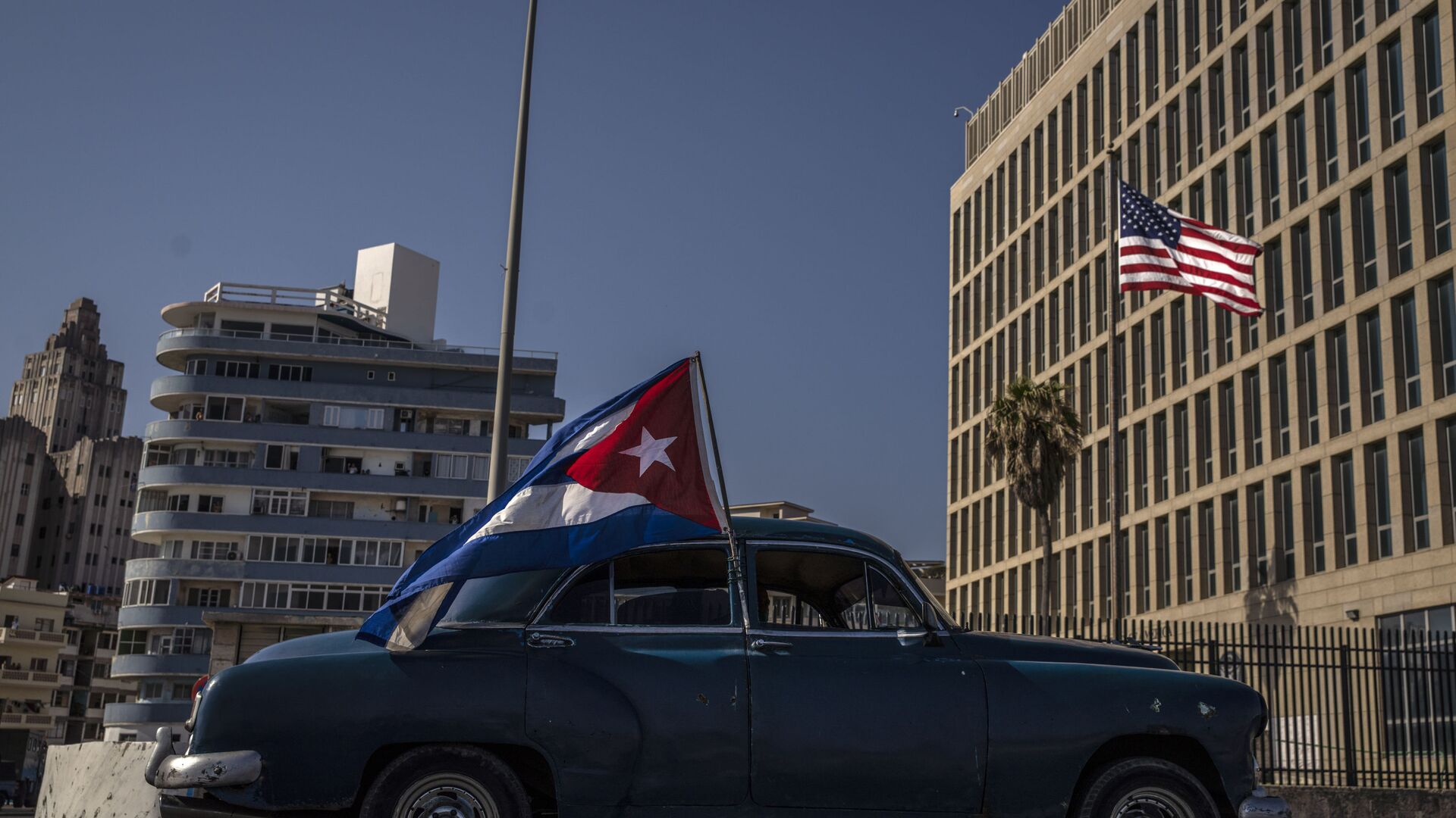 A classic American car flying a Cuban flag drives past the American embassy during a rally calling for the end of the US blockade against the island nation, in Havana, Cuba, Sunday, March 28, 2021. - Sputnik International, 1920, 14.11.2021