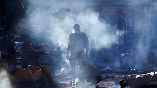 A family member wearing personal protective equipment (PPE) stands next to a body of a person, who died from the coronavirus disease (COVID-19), before their cremation, at a crematorium in New Delhi, India April 24, 2021 - Sputnik International