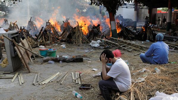 Family members sit next to the burning funeral pyres of those who died from the coronavirus disease (COVID-19), during a mass cremation, at a crematorium in New Delhi, India April 26, 2021 - Sputnik International