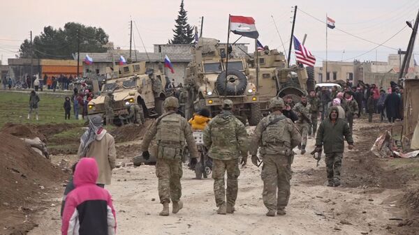 In this frame grab from video, Russian, Syrian and others gather next to an American military convoy stuck in the village of Khirbet Ammu, east of Qamishli city, Syria, Wednesday, Feb. 12, 2020. The Syrian official news agency SANA, said Wednesday, that locals had gathered at an army checkpoint, pelting the U.S. convoy with stones and taking down a U.S. flag flying on a vehicle when troops fired with live ammunition and smoke bombs. (AP Photo) - Sputnik International