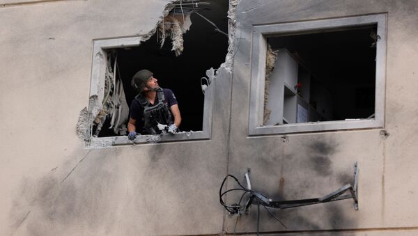 An Israeli police bomb disposal expert looks out from the window of a residential building that was damaged after it was hit by a rocket launched from the Gaza Strip, in Ashkelon, southern Israel May 11, 2021.  - Sputnik International