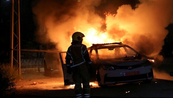 An Israeli firefighter stands near a burning Israeli police car during clashes between Israeli police and members of the country's Arab minority in the Arab-Jewish town of Lod, Israel May 12, 2021. - Sputnik International