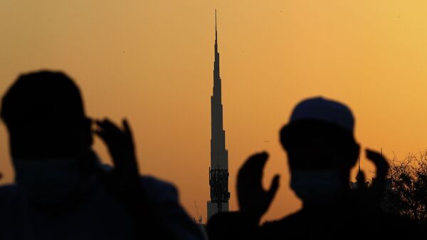 На фоне самого высокого здания в мире, Бурдж-Халифа, мусульманские мужчины в масках молятся, Дубай - Sputnik International