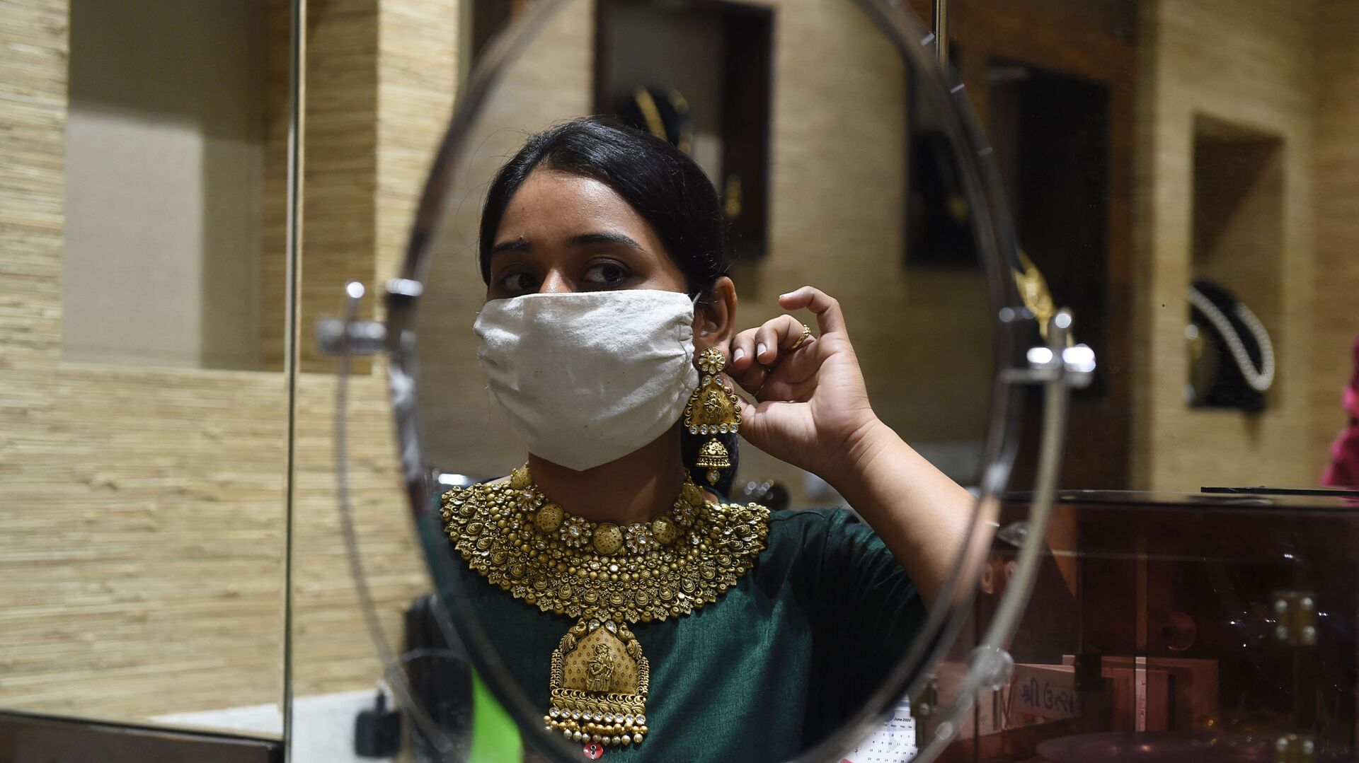 A customer wearing a face mask as a preventive measure against the COVID-19 coronavirus, looks herself in the mirror while trying on gold jewelry in an Ahmedabad shop on July 31, 2020. - Sputnik International, 1920, 18.04.2022
