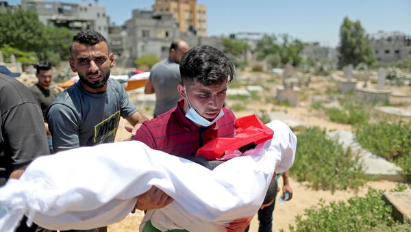 A man carries the body of a Palestinian child from Al-Hadidi family, who was killed amid a flare-up of Israeli-Palestinian violence, during their funeral at a cemetery in the northern Gaza Strip May 15, 2021. - Sputnik International