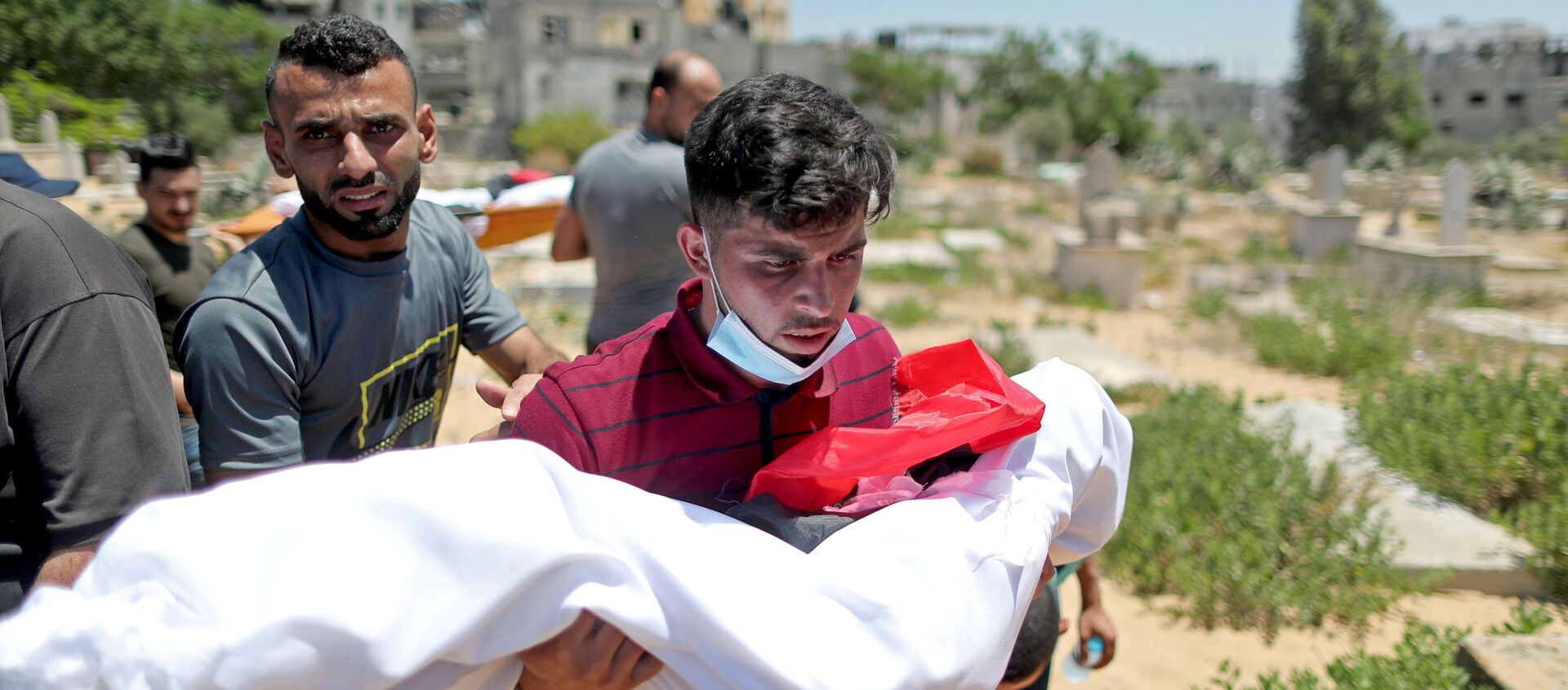 A man carries the body of a Palestinian child from Al-Hadidi family, who was killed amid a flare-up of Israeli-Palestinian violence, during their funeral at a cemetery in the northern Gaza Strip May 15, 2021. - Sputnik International, 1920