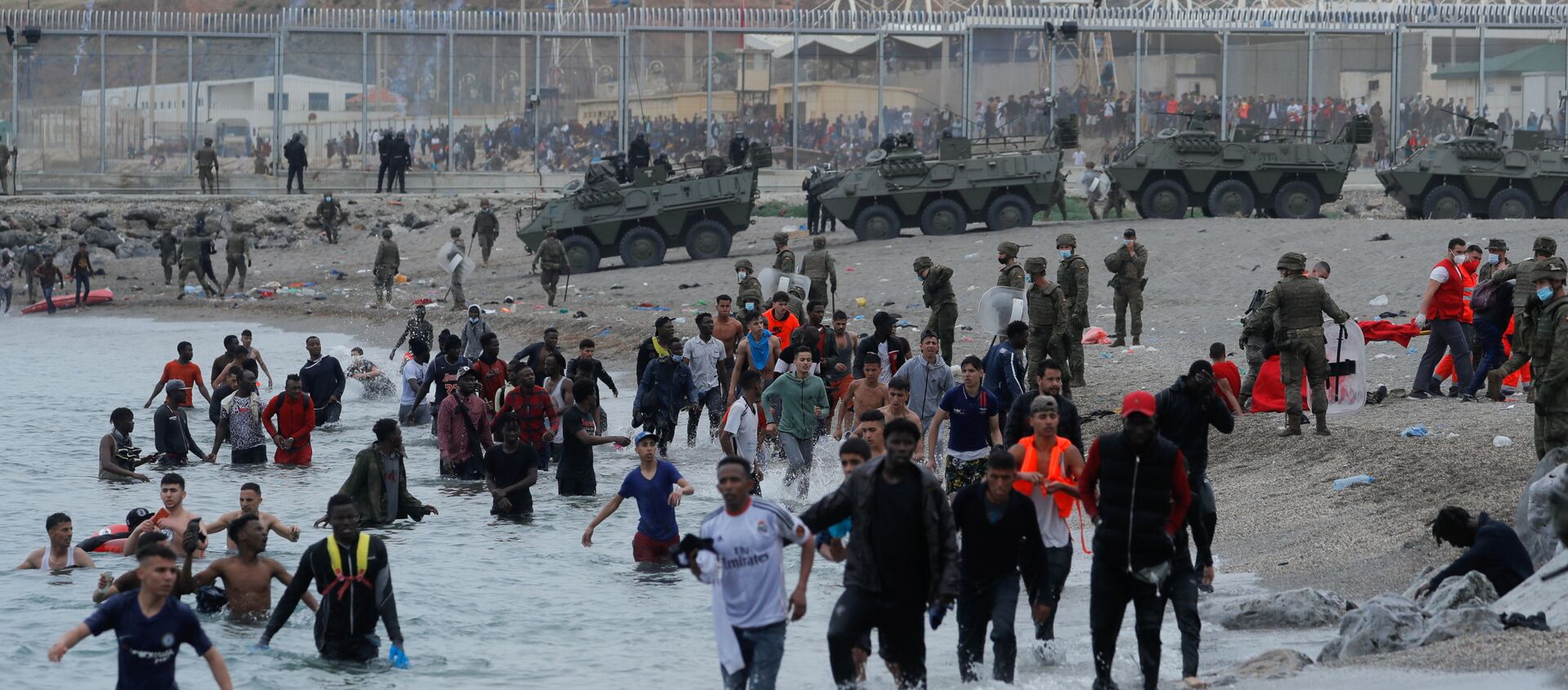Moroccan citizens walk in the water as Spanish legionnaires patrol the area near the fence on a beach in El Tarajal, after thousands swam across the Spanish-Moroccan border on Monday, in Ceuta, Spain, May 18, 2021. REUTERS/Jon Nazca - Sputnik International, 1920, 18.05.2021