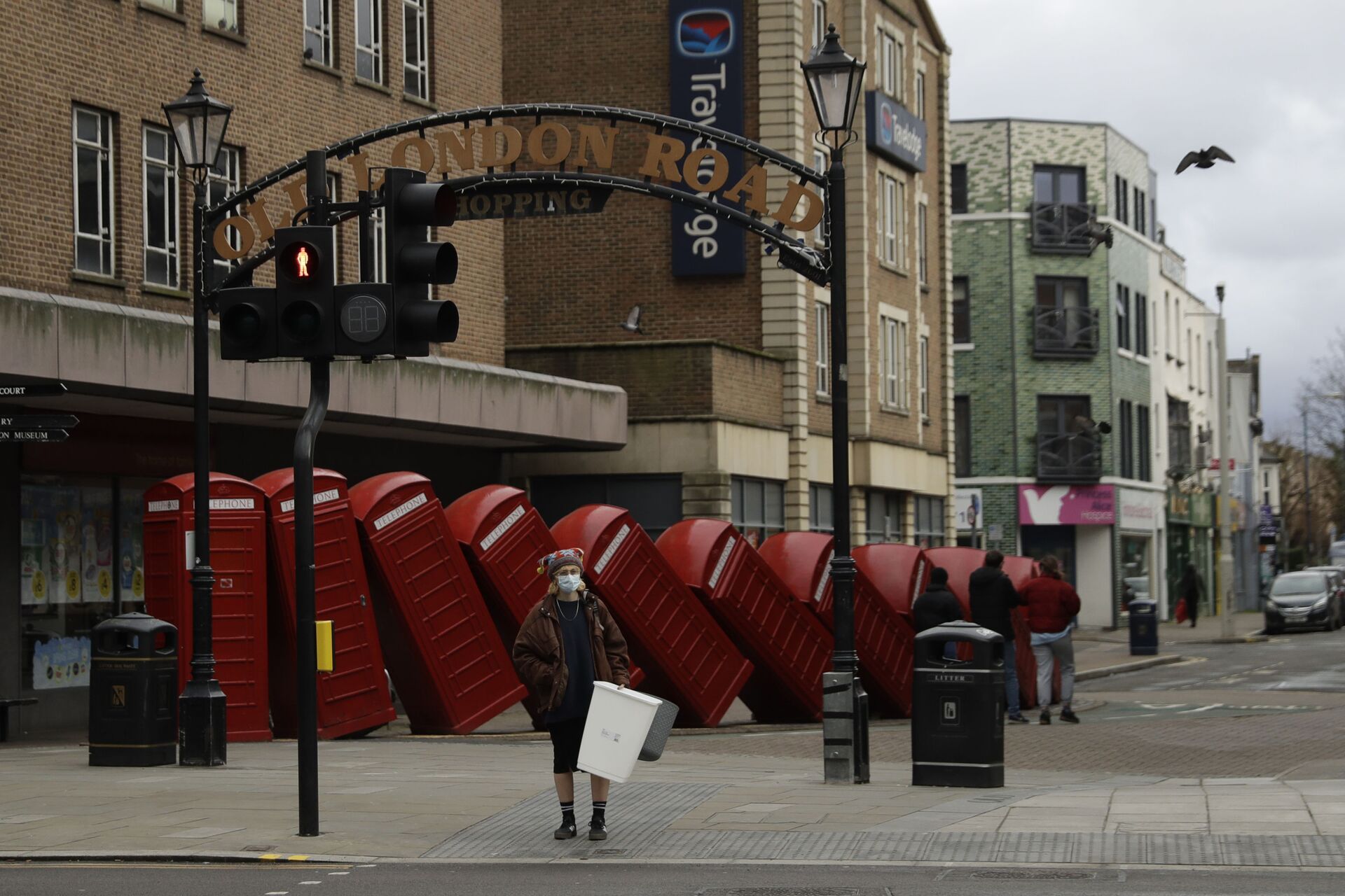 A woman wearing a face mask to curb the spread of coronavirus waits to cross the street backdropped by Out of Order a 1989 red phone box sculpture by British artist David Mach, in Kingston upon Thames, south west, London, Tuesday, Jan. 19, 2021 - Sputnik International, 1920, 07.09.2021
