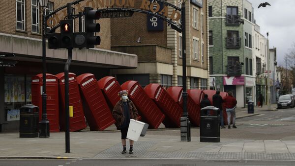 A woman wearing a face mask to curb the spread of coronavirus waits to cross the street backdropped by Out of Order a 1989 red phone box sculpture by British artist David Mach, in Kingston upon Thames, south west, London, Tuesday, Jan. 19, 2021 - Sputnik International