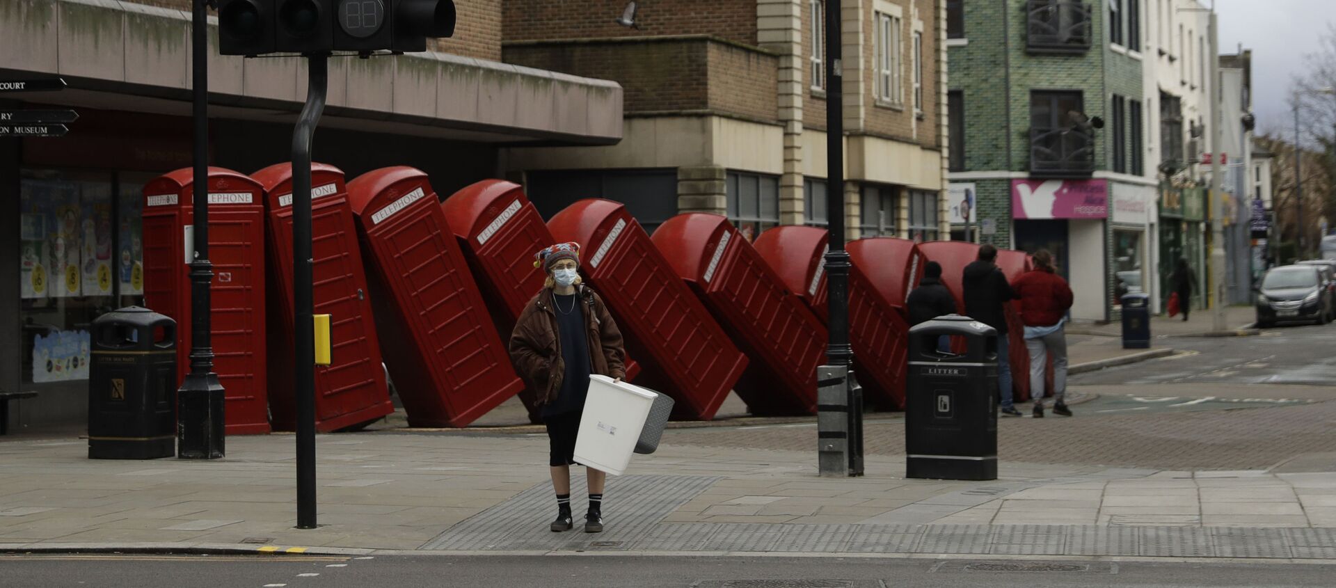 A woman wearing a face mask to curb the spread of coronavirus waits to cross the street backdropped by Out of Order a 1989 red phone box sculpture by British artist David Mach, in Kingston upon Thames, south west, London, Tuesday, Jan. 19, 2021 - Sputnik International, 1920