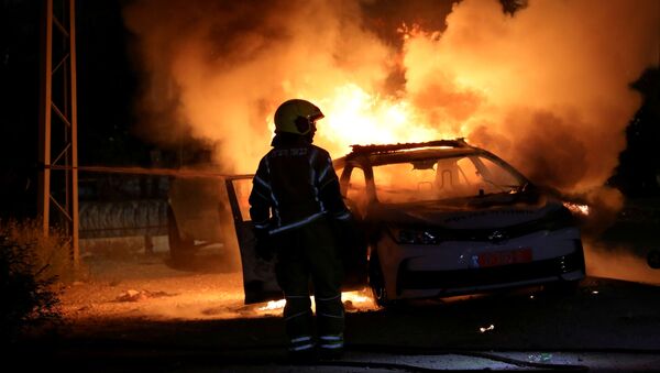 An Israeli firefighter stands near a burning Israeli police car during clashes between Israeli police and members of the country's Arab minority in the Arab-Jewish town of Lod, Israel May 12, 2021 - Sputnik International