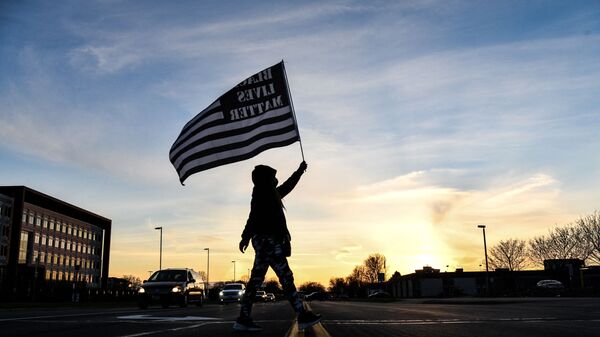 A demonstrator marches, holding a Black Lives Matter flag, during the sixth night of protests over the shooting death of Daunte Wright by a police officer in Brooklyn Center, Minnesota on April 16, 2021 - Sputnik International