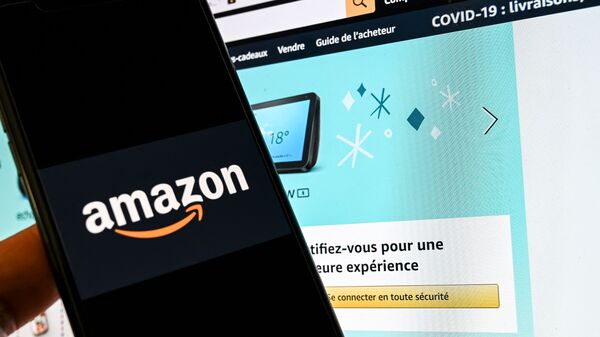 In this photograph taken on November 18, 2020 in Lille, a person poses with a smartphone showing an Amazon logo, in front of a computer screen displaying the home page of Amazon France sales website. - Sputnik International