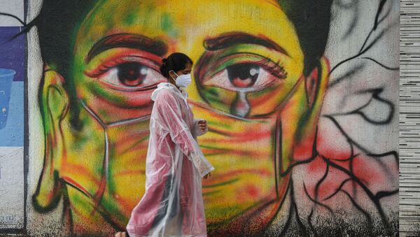 A woman wearing a raincoat walks past a mural depicting a woman with a facemask to spread awareness about the Covid-19 coronavirus, in Mumbai on June 17, 2021 - Sputnik International