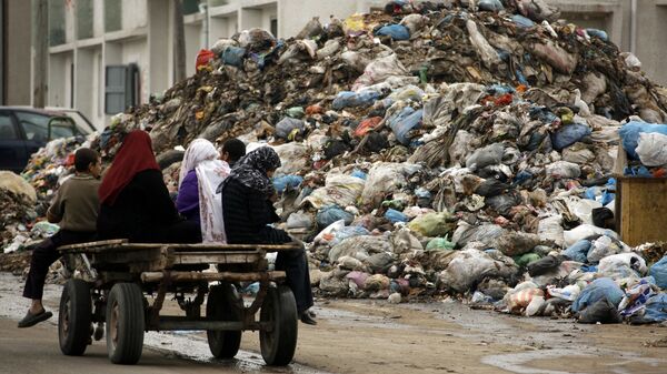 Palestinian women riding a donkey cart drive past a garbage dump in Beit Lahia on the Gaza Strip on January 20, 2009. The garbage has started to pill up in the streets as municipality services are still not available. (Photo by PATRICK BAZ / POOL / AFP) - Sputnik International