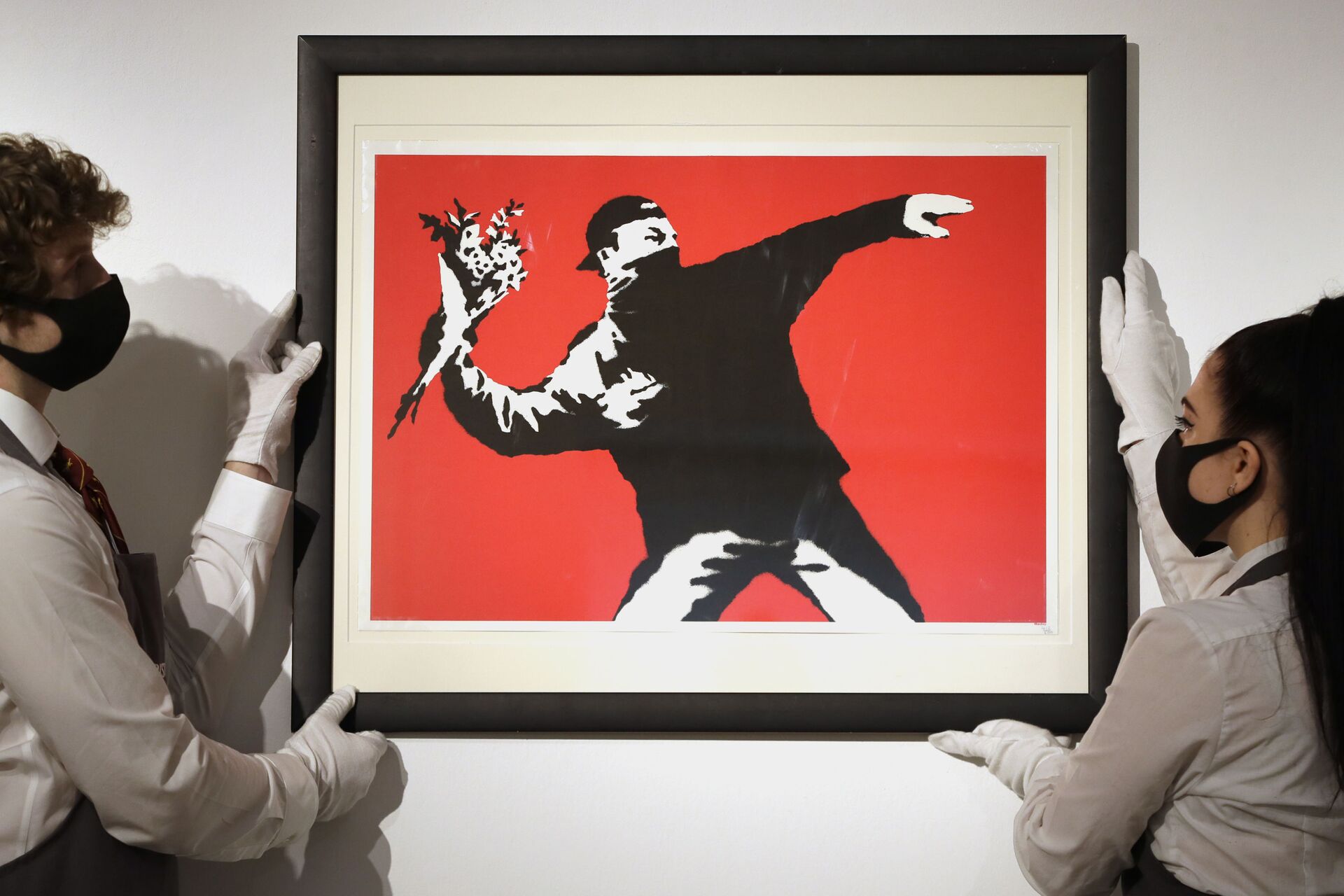 Gallery technicians display a Banksy called Love is in the Air screenprint in colours, 2003, on wove paper, numbered 412/500 in pencil at Christie's auction rooms in London, Friday, March 26, 2021 - Sputnik International, 1920, 03.01.2023