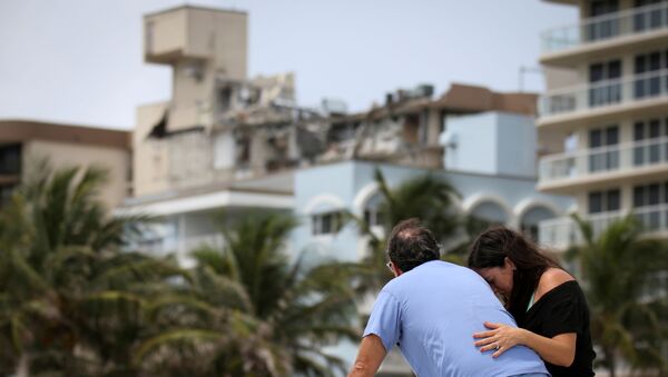 A couple at the beach reacts near the partially collapsed residential building as the emergency crews continue search and rescue operations for survivors, in Surfside, near Miami Beach, Florida, U.S. June 26, 2021. - Sputnik International