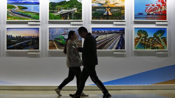 In this Saturday, April 27, 2019 file photo, people walk by a display board showcasing China's sweeping infrastructure-building projects at the media center of the Belt and Road Forum in Beijing - Sputnik International