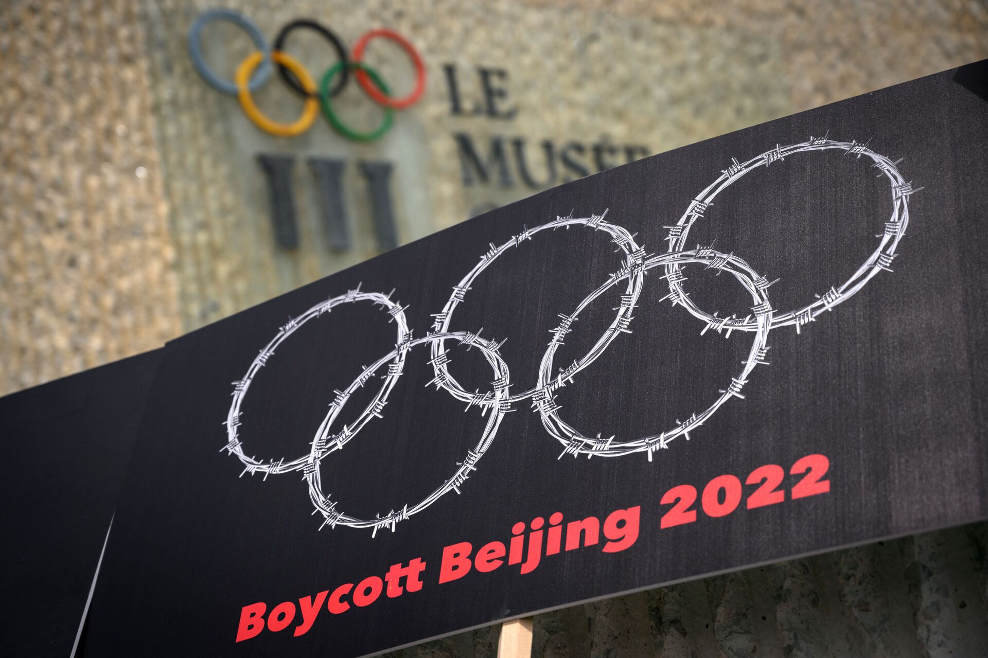 This photograph taken on June 23, 2021 shows a placard representing barber wire shaping and Olympics Rings are seen next to a sign of the Olympics Museum during a protest organised by Tibetan and Uyghur activists against Beijing 2022 Winter Olympics, in Lausanne as some 200 participants took part to the protest.  - Sputnik International, 1920, 06.12.2021
