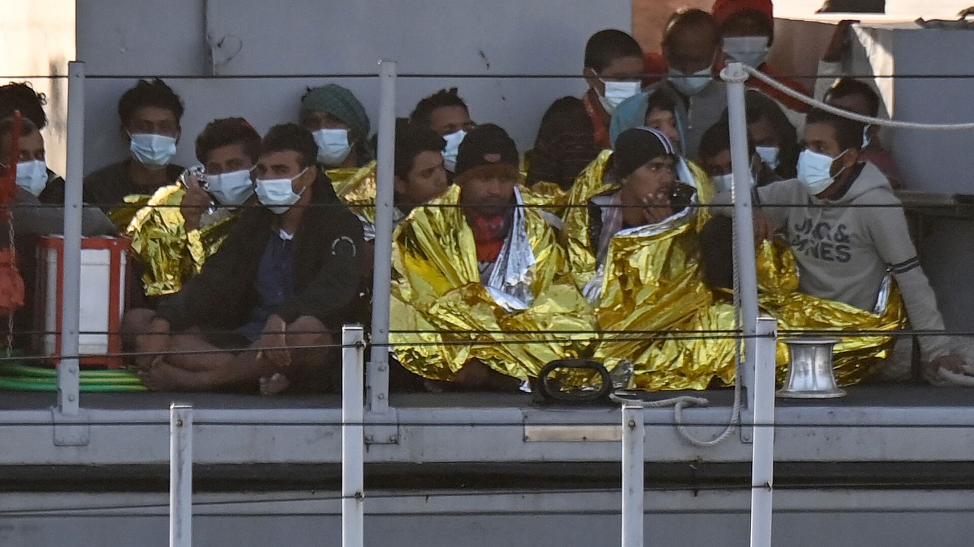 Migrants warmed by emergency blankets arrive on a boat of the Italian Guardia Di Finanza law enforcement agency on May 17, 2021 to disembark on the southern Italian Pelagie Island of Lampedusa. - More than 1,400 migrants arrived on the Italian island of Lampedusa at the weekend, sparking calls from far-right politicians for action to stem the flow, amid fresh moves by Italian authorities against the rescue boats who operate in the central Mediterranean. - Sputnik International, 1920, 14.09.2023
