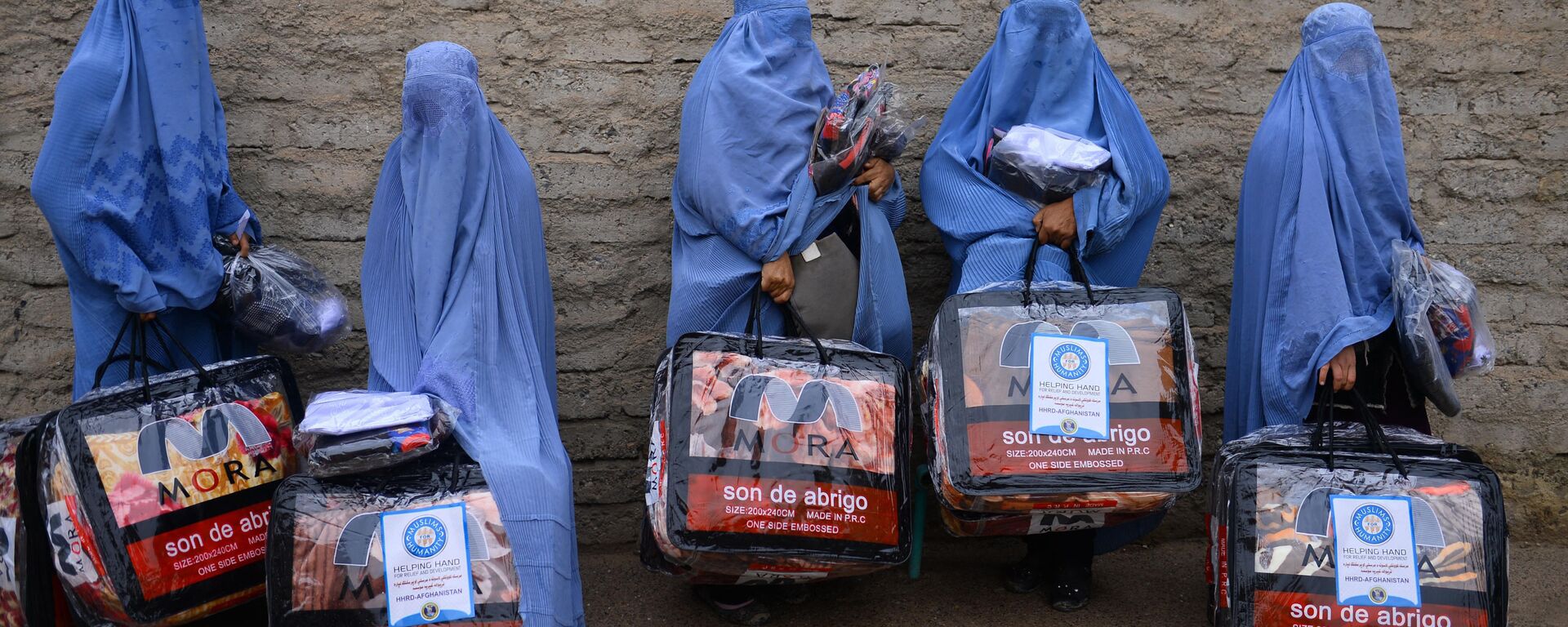 In this photograph taken on December 19, 2019, Afghan burqa-clad women stand with aid items recieved from a charity in Herat. - Sputnik International, 1920, 10.07.2021