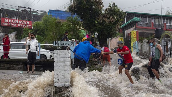 People help each other cross a street amid sudden gush of water during flash floods after heavy monsoon rains in Bhagsunag, a popular tourist town in Himachal Pradesh, India, Monday, July 12, 2021 - Sputnik International