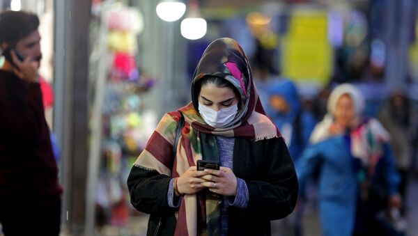 An Iranian woman wearing a protective mask checks her mobile telephone as she walks in a street in the capital Tehran on February 20,2020 (Photo by ATTA KENARE / AFP) - Sputnik International