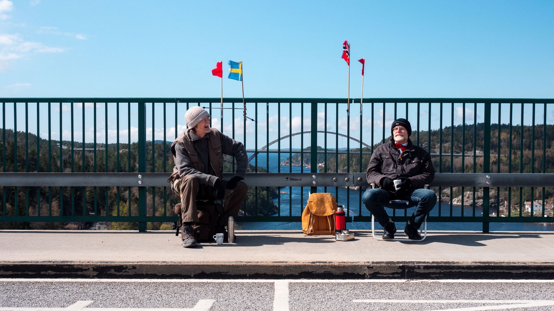 Pontus Berglund (L) sits on the Swedish side while his brother Ola sits on the Norwegian side of the old bridge of Svinesund with the respective country flags and the new Svinesund Bridge in the background, in Svinesund, Norway  and Sweden, on May 1, 2021 - Sputnik International, 1920, 02.02.2022