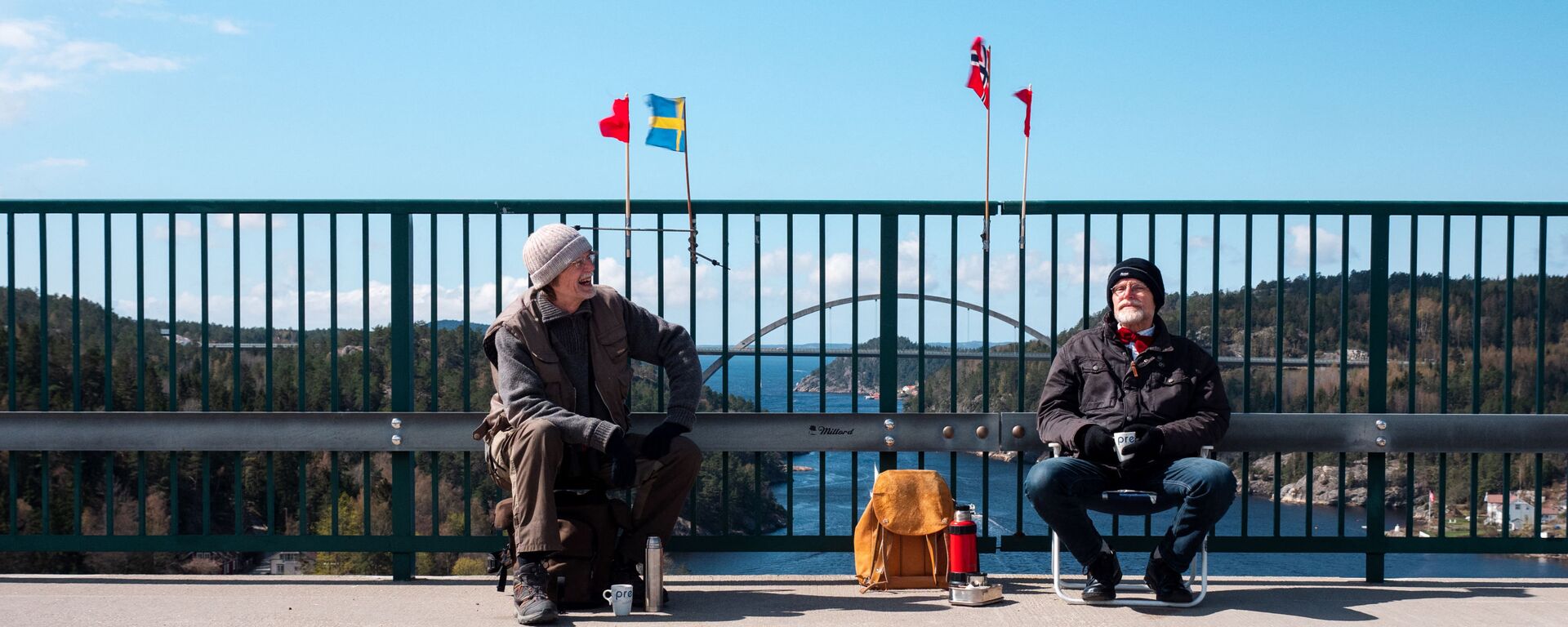 Pontus Berglund (L) sits on the Swedish side while his brother Ola sits on the Norwegian side of the old bridge of Svinesund with the respective country flags and the new Svinesund Bridge in the background, in Svinesund, Norway  and Sweden, on May 1, 2021 - Sputnik International, 1920, 02.02.2022
