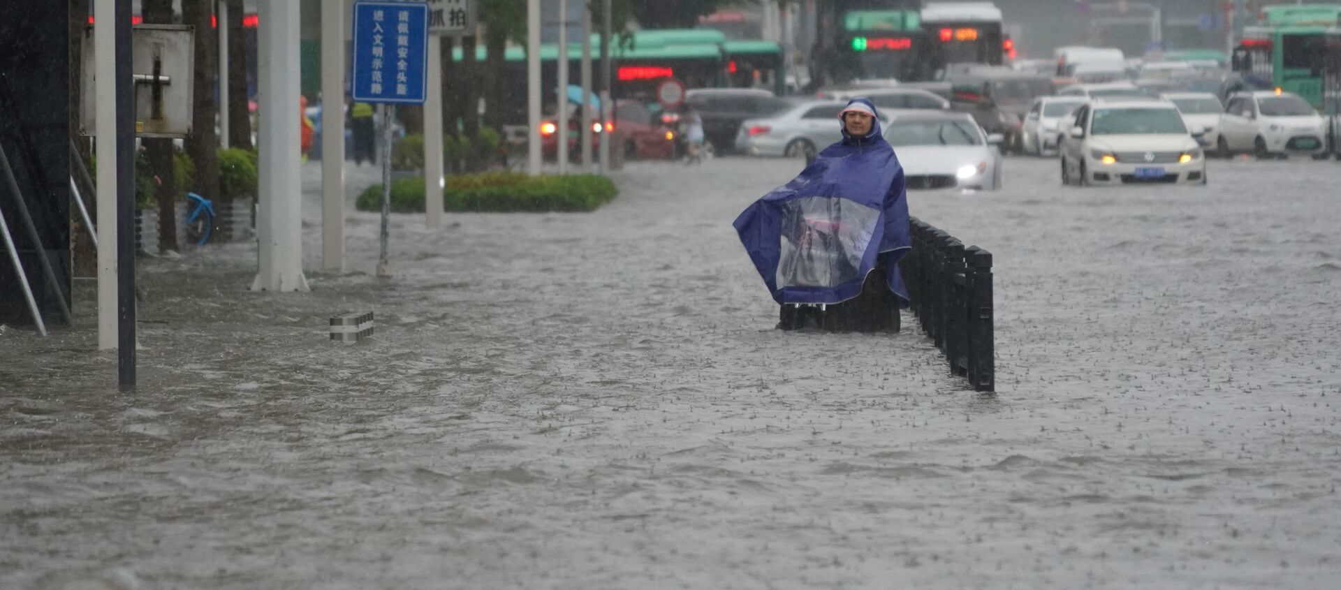 A resident wearing a rain cover stands on a flooded road in Zhengzhou, Henan province, China July 20, 2021. - Sputnik International, 1920, 20.07.2021