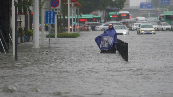 A resident wearing a rain cover stands on a flooded road in Zhengzhou, Henan province, China July 20, 2021. - Sputnik International