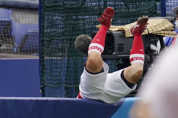 Yu Yamamoto of Japan falls over a wall after reaching for a foul ball hit by American Amanda Chidester in the sixth inning of a softball game at the Tokyo 2020 Olympics. - Sputnik International