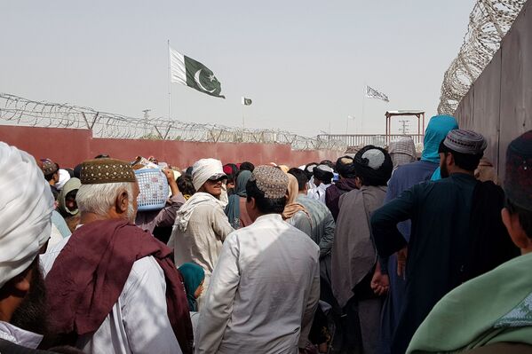 Pakistan's flag and the Taliban's flag are seen in the background as people make their way to Afghanistan at the Friendship Gate crossing point in the Pakistan-Afghanistan border town of Chaman, Pakistan, 15 August 2021. - Sputnik International