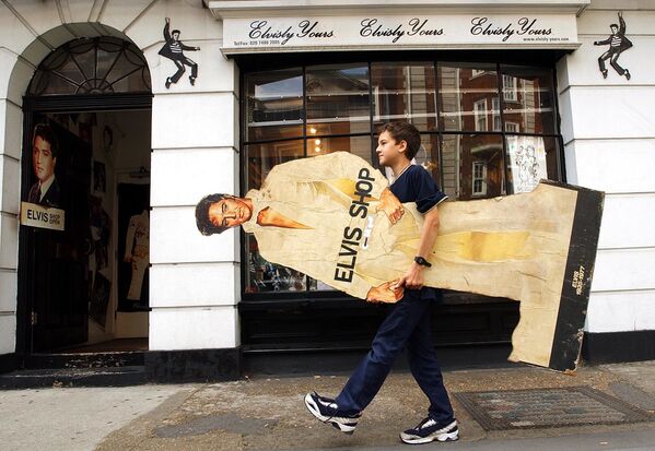 12-year-old Kostya Abramovich carries a large cut-out of Elvis Presley into a shop dedicated to the rock and roll legend named “Elvisly Yours” in central London on Friday, 16 August 2002. The shop was expecting greater turnover due to it being the 25th anniversary of his death on Friday. - Sputnik International