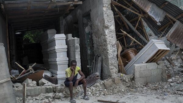 A man sits in front of a collapsed funeral home in Les Cayes, Haiti, Monday, Aug. 16, 2021, two days after a 7.2-magnitude earthquake struck the southwestern part of the country. - Sputnik International