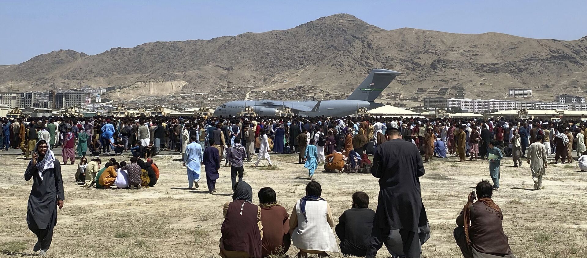 Hundreds of people gather near a U.S. Air Force C-17 transport plane at a perimeter at the international airport in Kabul, Afghanistan, Monday, Aug. 16, 2021. On Monday, the U.S. military and officials focus was on Kabul’s airport, where thousands of Afghans trapped by the sudden Taliban takeover rushed the tarmac and clung to U.S. military planes deployed to fly out staffers of the U.S. Embassy, which shut down Sunday, and others - Sputnik International, 1920
