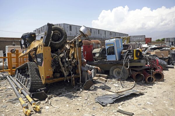 In this 3 May 2021 file photo, a man rests in the shade of destroyed machinery sold by the US military to a scrapyard, outside Bagram Air Base, in Afghanistan. - Sputnik International