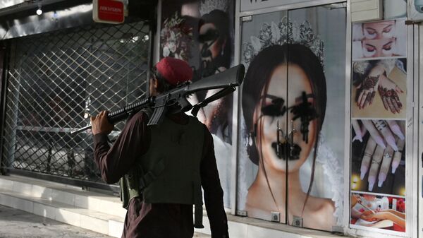 (FILES) In this file photo taken on August 18, 2021, a Taliban fighter walks past a beauty salon with images of women defaced using spray paint in Shar-e-Naw in Kabul - Sputnik International