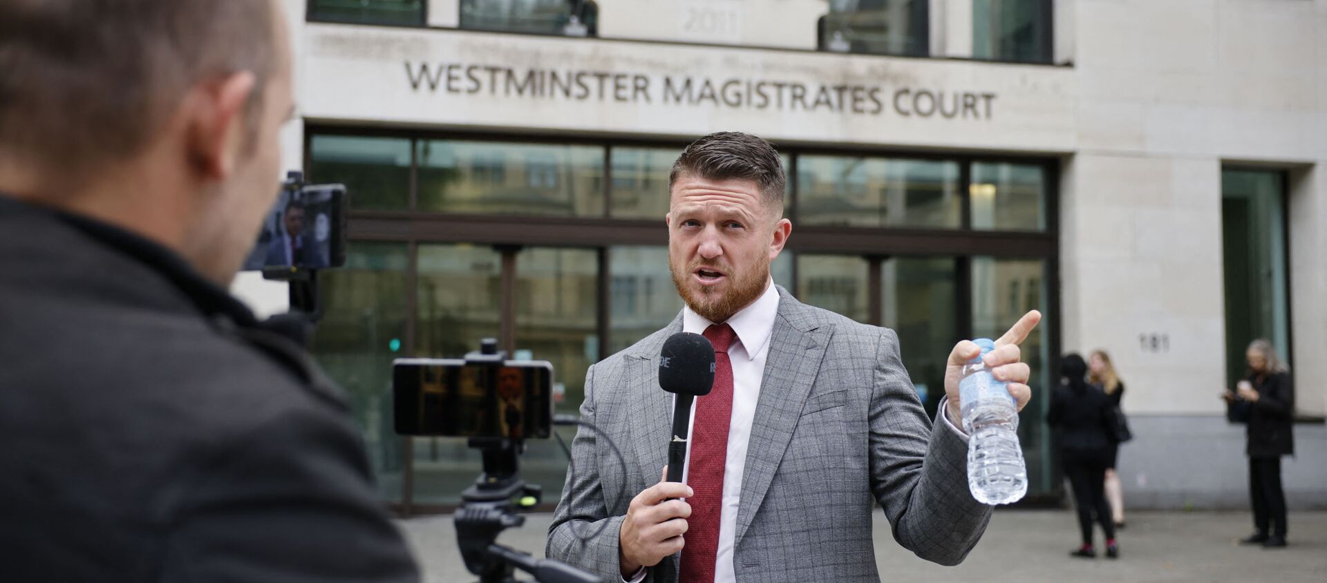 Founder and former leader of the anti-Islam English Defence League (EDL), Stephen Yaxley-Lennon, AKA Tommy Robinson, speaks to a camera as he arrives at Westminster Magistrates Court in central London on August 20, 2021 for a hearing after an application for a stalking protection order against him was filed.  - Sputnik International, 1920, 21.08.2021